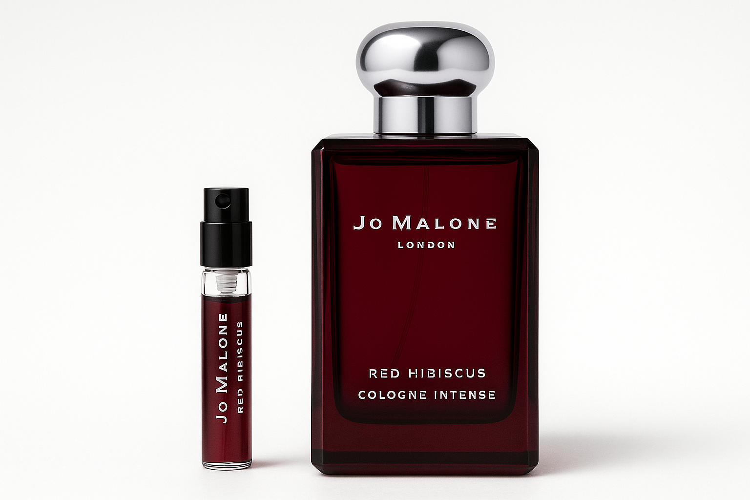 Jo Malone Red Hibiscus Cologne Intense 2 ml-es minta áll egy 100 ml-es Jo Malone Red Hibiscus Cologne Intense parfümös üveg mellett, amelyen fehér felirat látható a sötétvörös üvegen.