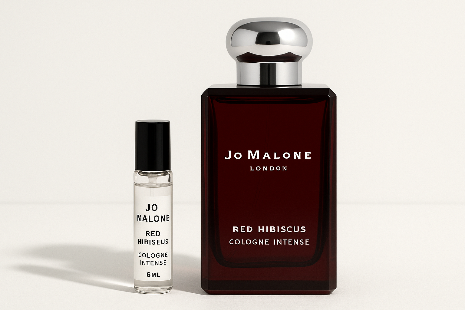 Jo Malone Red Hibiscus Cologne Intense 6 ml-es minta, mellette egy 100 ml-es Jo Malone Red Hibiscus Cologne Intense parfümös üveg, amelyen fehér felirat látható a sötétvörös üvegen.